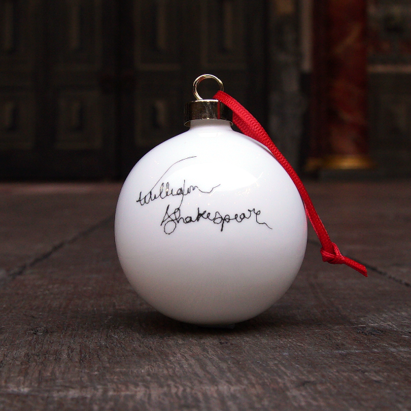 White fine china hanging bauble with a gold ferule and red ribbon. On the bauble is a portrait of William Shakespeare based on an embroidery. The portrait is made up of black lines and has a scribbled look.