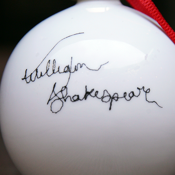 White fine china hanging bauble with a gold ferule and red ribbon. On the bauble is a portrait of William Shakespeare based on an embroidery. The portrait is made up of black lines and has a scribbled look.