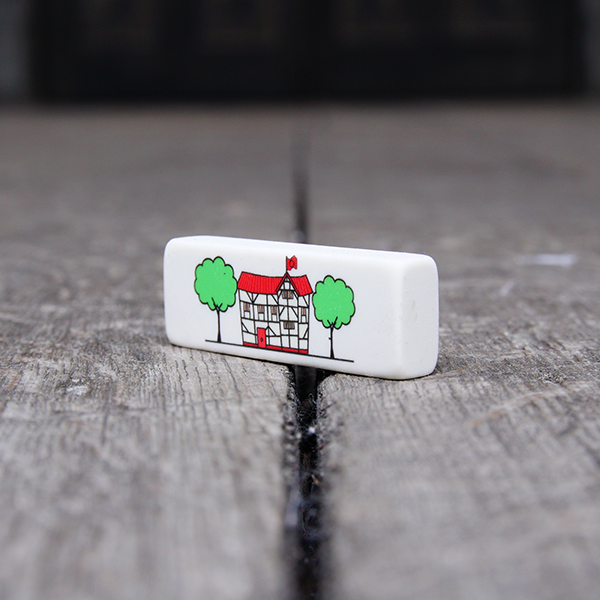 Rectangular white eraser with a print of an illustration of the Globe Theatre in black outline. The theatre also has a red roof and door and is flanked by two green trees.