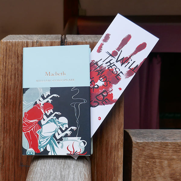 Large white card bookmark with an image of a bloody handprint. Over the hand print is a quote from Shakespeare play, Macbeth, printed in black hand-drawn lettering. Shown with a copy of the Collector's Library 'Macbeth'