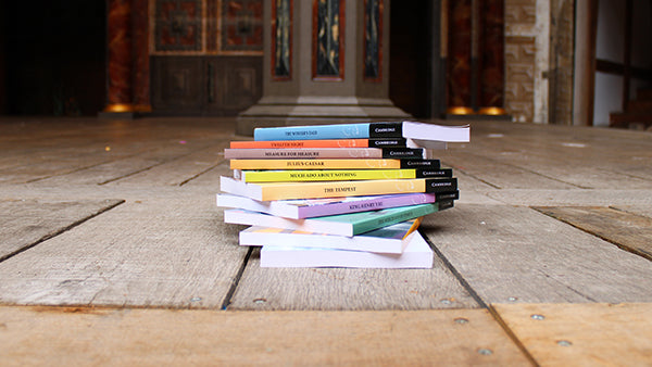 Stack of paperback books with various pastel coloured spines on top of wooden stage planks