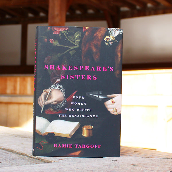 Hardback book with a dark cover and a image of a person holding a feather quill and writing in a book. Bright Pink writing states the title of the book and the author's name, "Shakespeare's Sisters" by Ramie Targoff.