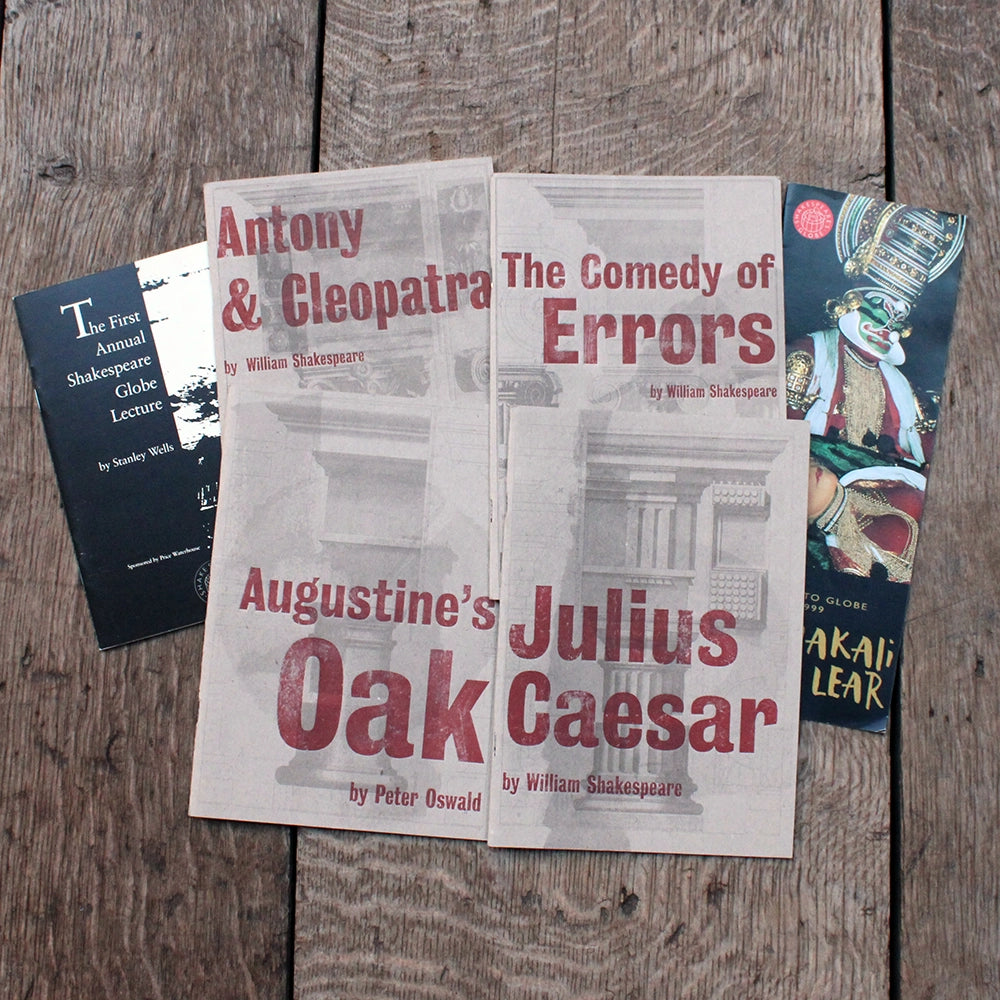 Four theatre programmes with grey covers and red titles on a wooden background