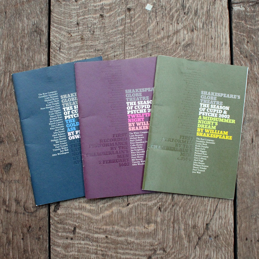 Three theatre programmes, one with a blue cover, one with a burgundy red cover and one with a green cover, on a wooden background