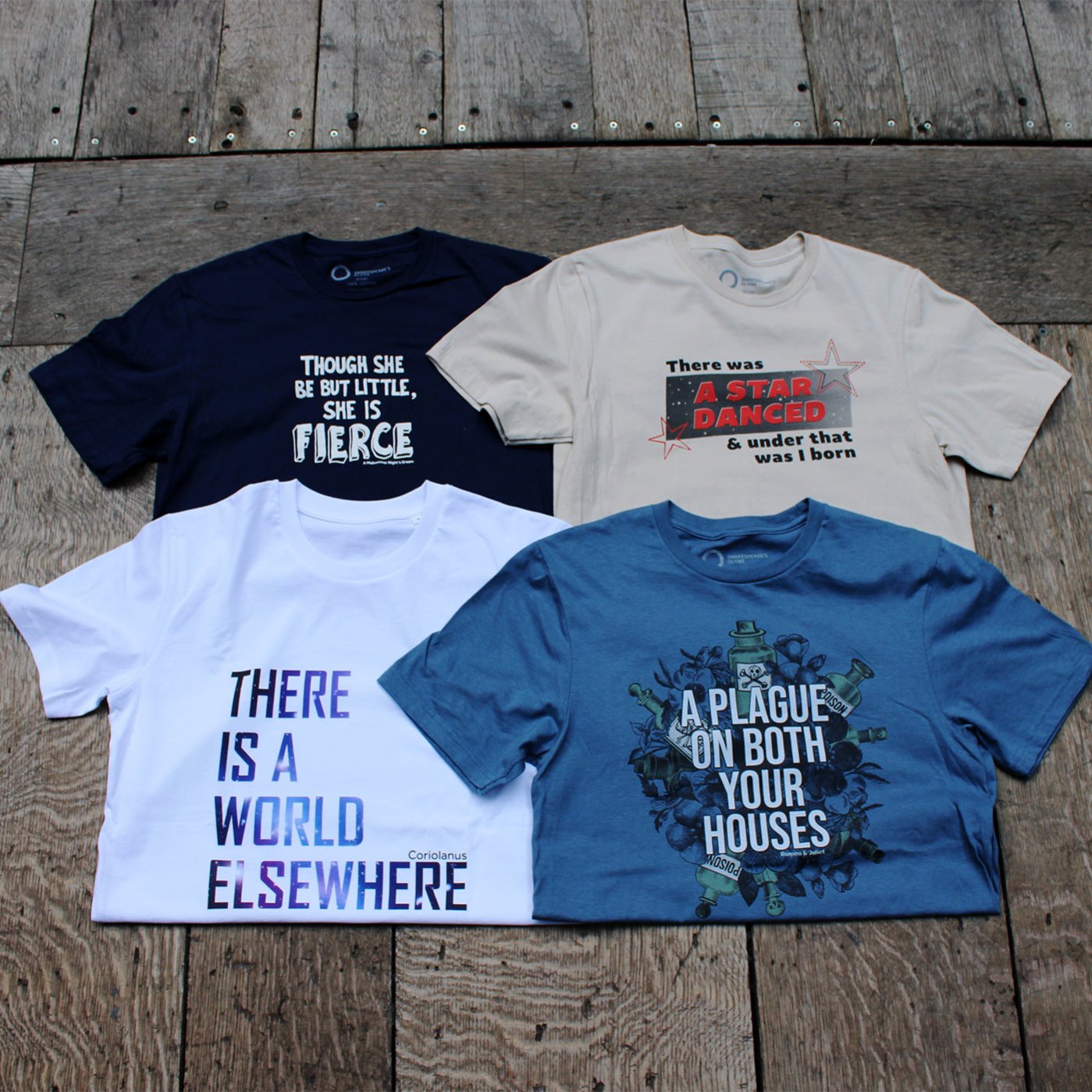 Wood panel stage floor with 5 graphic t-shirts laid across it, from left, black, navy blue, beige, white, pale blue