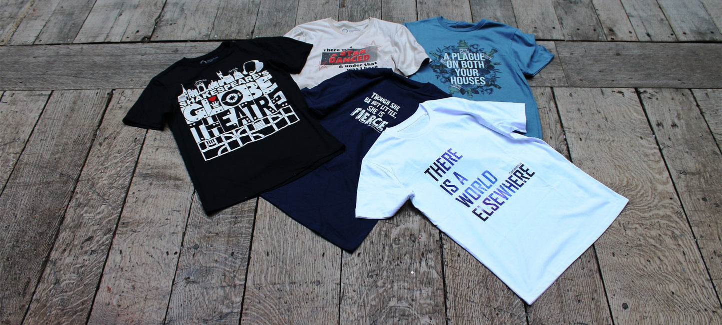 Wood panel stage floor with 5 graphic t-shirts laid across it, from left, black, navy blue, beige, white, pale blue