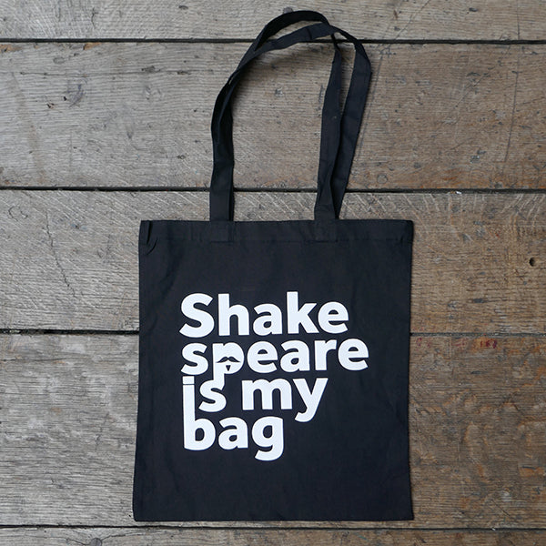 Black cotton bag with mid-length handles, printed with white text.  On a wooden board background