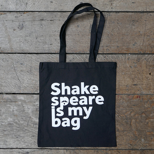 
                  
                    Black cotton bag with mid-length handles, printed with white text.  On a wooden board background
                  
                