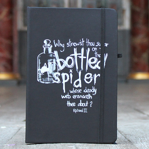 Black hardback notebook with black elastic closure on right side, featuring white scratchy graphic text