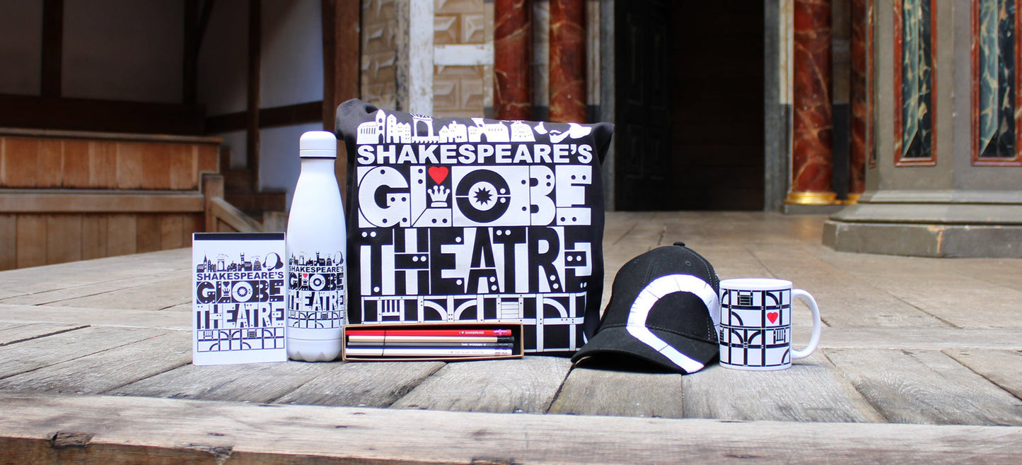 Black and white Globe Theatre range gifts sitting on Globe stage, from left to right, paperback notepad, water bottle, tote bag, pencil box, baseball cap, mug