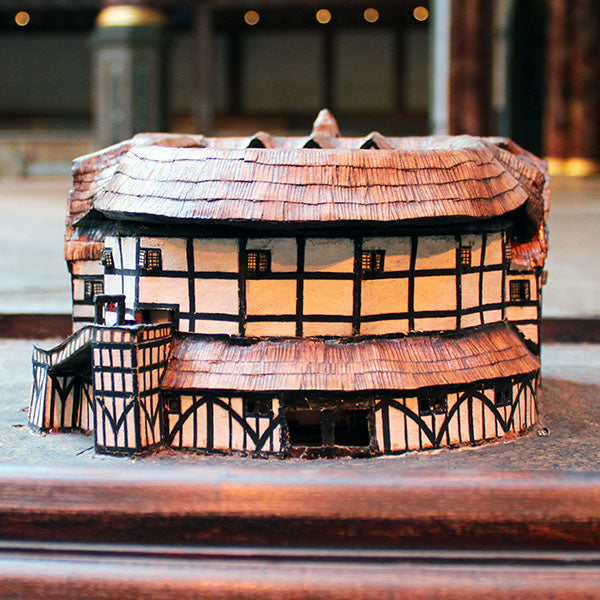 Model of a half-timbered theatre with a thatched roof on a wooden surface.