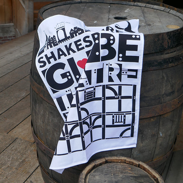 White cotton tea towel printed with black representations of timber-framed panels and the words Globe Theatre. There is a red heart printed in the middle