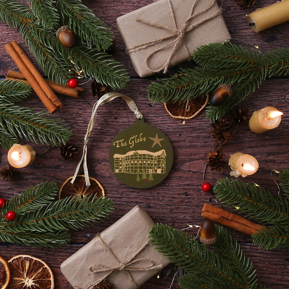 Green round wooden decoration with 'The Globe' and stylised drawing of the Globe Theatre on wooden background with Christmas greenery