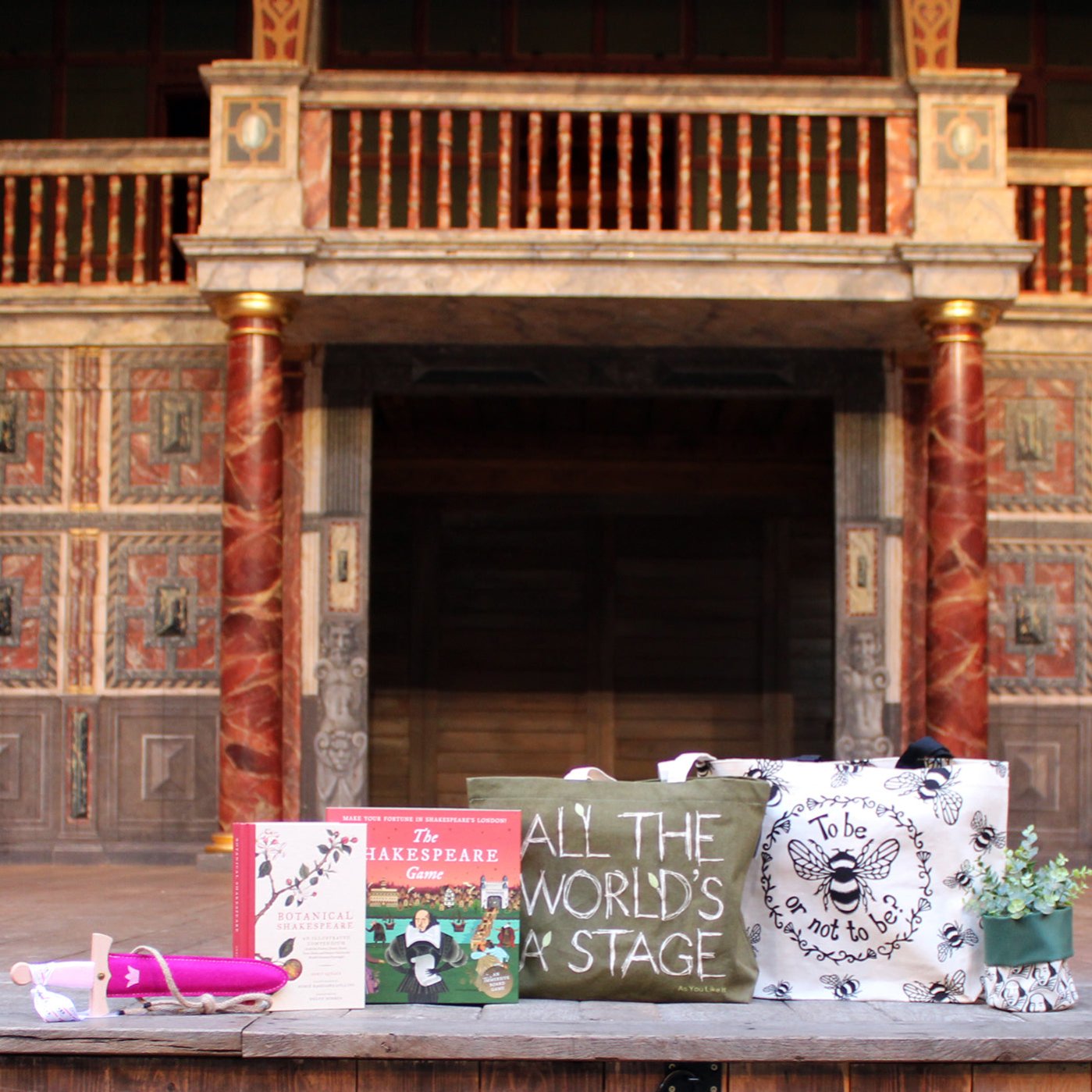 Selection of Green Friday sale items on Globe stage, from left to right, hardback book, dagger and sheath, board game, tote bag, tote bag, plant pot holder