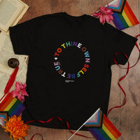 Black t-shirt with colorful text design on a wooden surface with rainbow flags and flowers.
