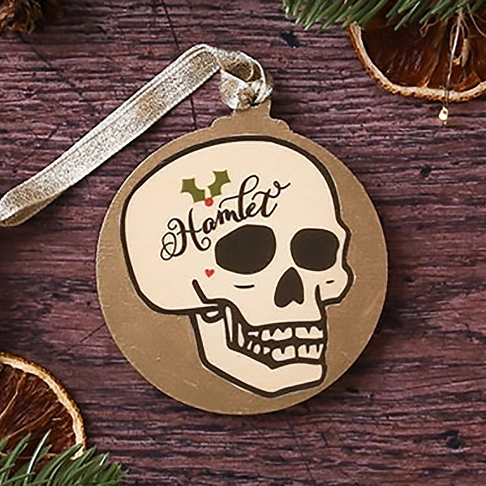 Round, flat, gold, Christmas decoration with Hamlet skull on it, on wooden background with Christmas greenery