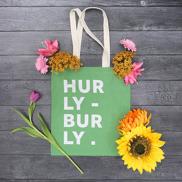 
                  
                    Lime green cotton tote bag with natural handles and white graphic text on front, featuring scattered flowers in background
                  
                