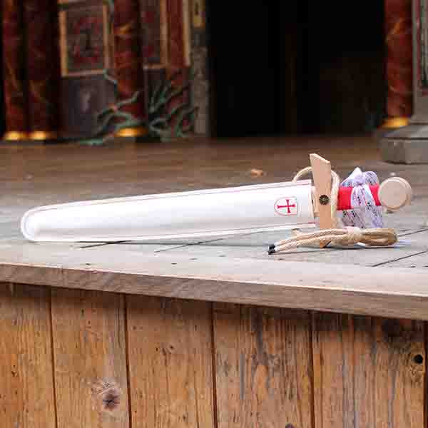 Wooden toy sword with a red handle and a white scabbard, sitting on a wooden stage
