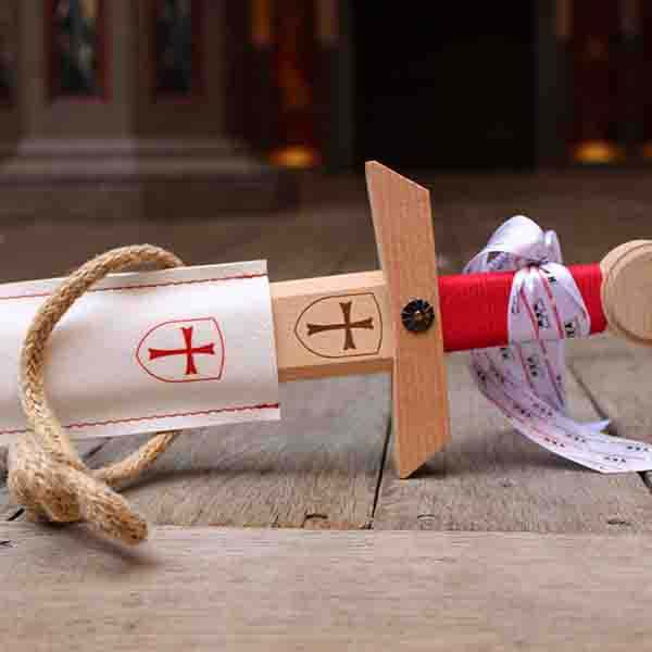 Wooden toy sword with a red handle and a white scabbard, sitting on a wooden stage