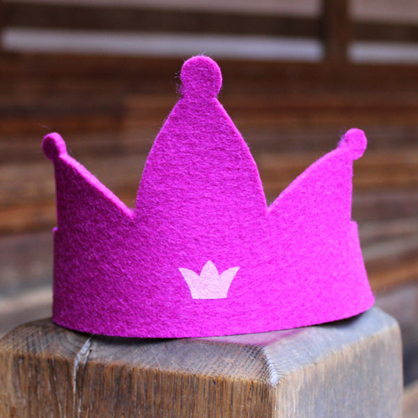 Bright pink felt crown with three points and a pale pink crown motif sitting on a wooden post.