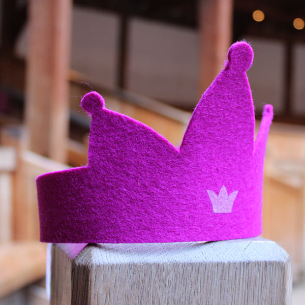 
                  
                    Bright pink felt crown with three points and a pale pink crown motif sitting on a wooden post.
                  
                