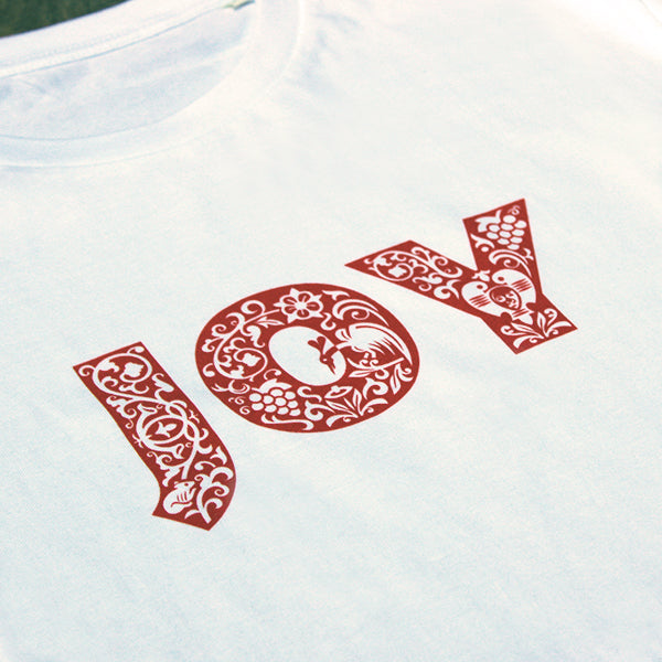 
                  
                    white t-shirt with a red patterned text print on the chest that reads JOY
                  
                