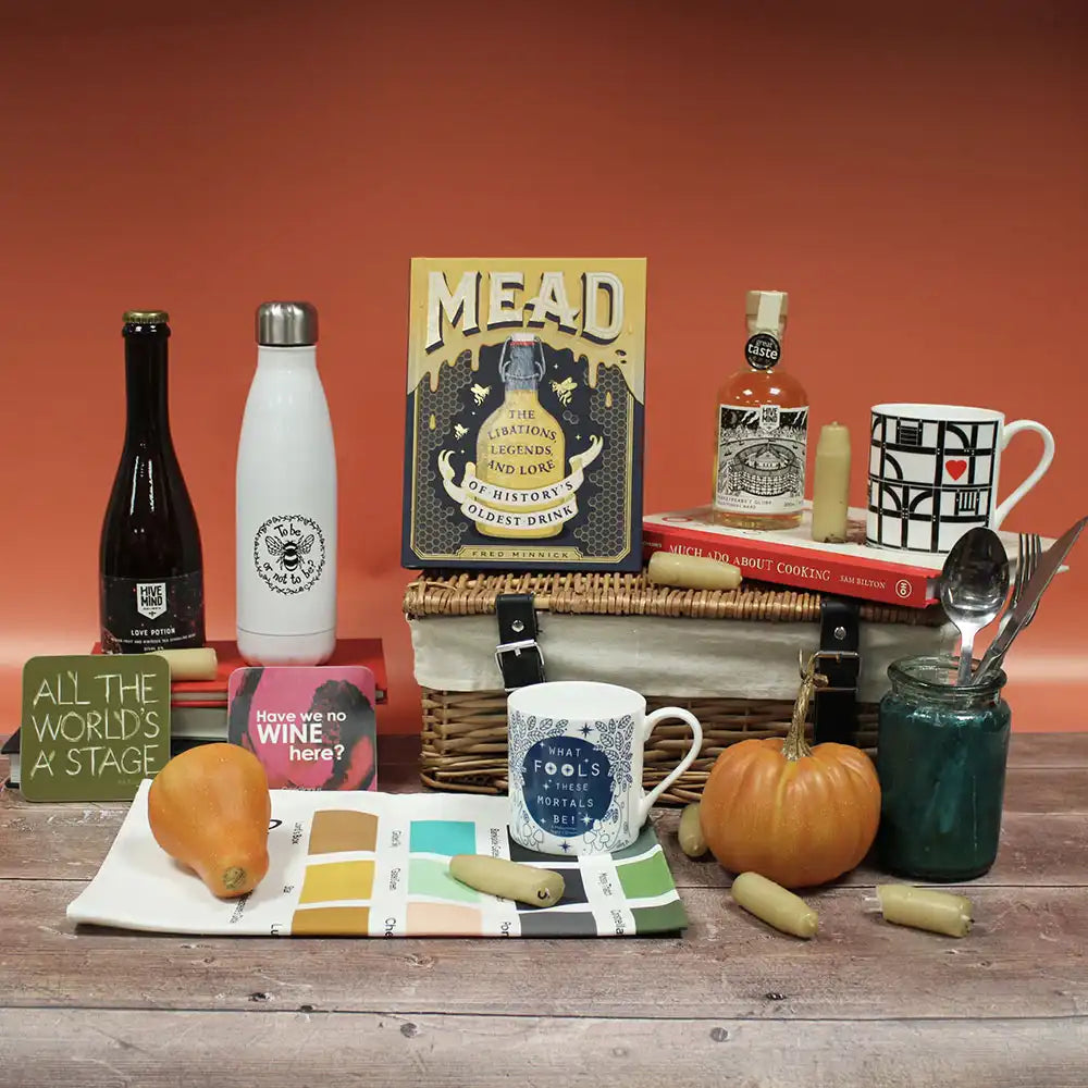 Tabletop display with mead bottles, water bottle, candles, tea towels, books, and mugs against a red background