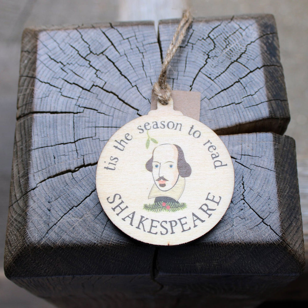 
                      
                        Round, flat, wooden Christmas decoration with Shakespeare's face in centre surrounded by 'tis the season to read' text.
                      
                    