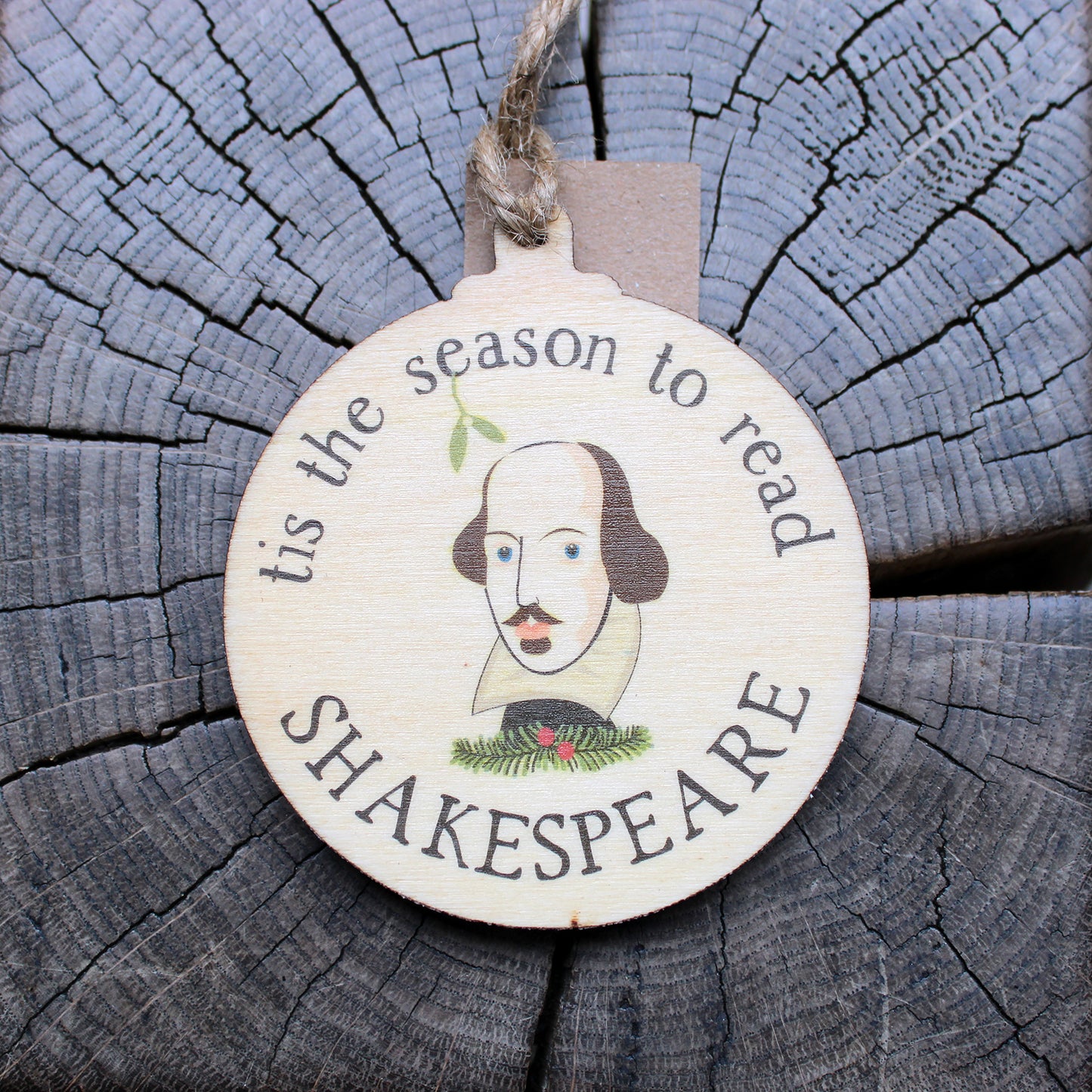 Round, flat, wooden Christmas decoration with Shakespeare's face in centre surrounded by 'tis the season to read' text.