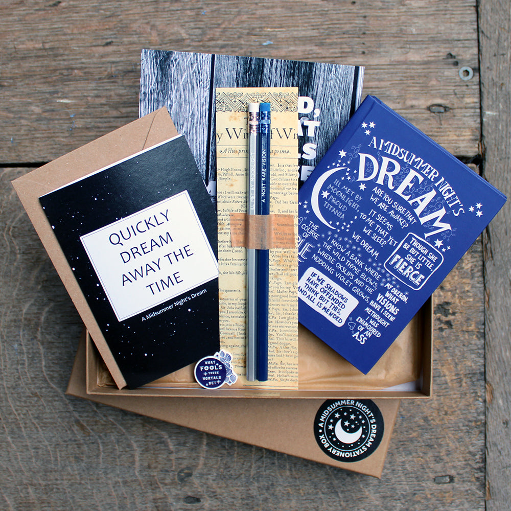 
                      
                        A kraft box with a black and white sticker in the bottom right corner, open with blue notebook, black greeting card, black mini print, blue and white pin badge and silver and blue pencil
                      
                    