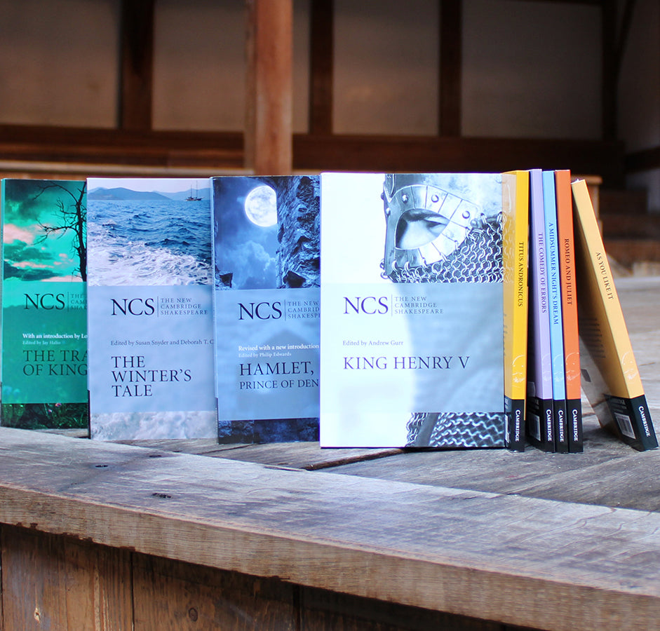 Paperback play texts standing up on wood panel stage, from left to right, teal, pale blue, blue, white, yellow, lilac, pale blue, orange, pale yellow