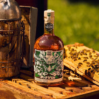 Bottle of 'Hive Mind' whisky barrel-aged mead on a wooden surface with a beehive and lantern in the background.