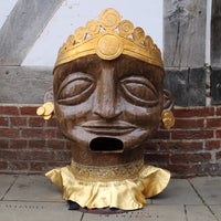 An Oshun headdress with a painted brown face and gold headdress, earrings and collar, displayed on the stone flagstones outside the Globe Theatre