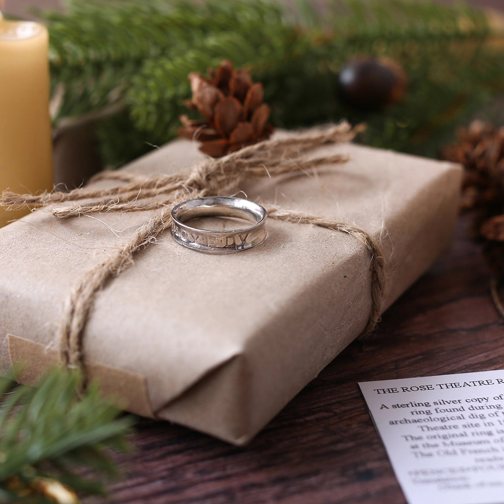 Engraved silver ring sitting on wrapped brown package, with Christmas greenery and lit candle