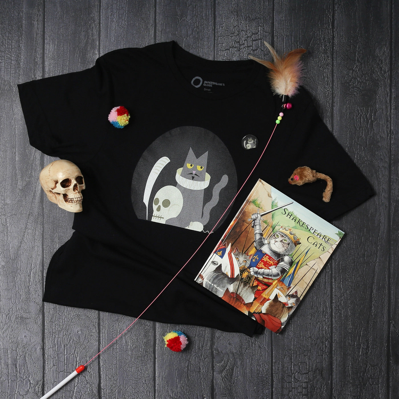 Grey panel wood flood with black graphic t-shirt with Shakespeare cat print and red, green, yellow, red paperback Shakespeare cats book