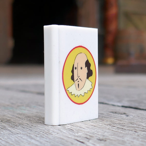 White eraser in the shape of a book printed with a cartoon portrait of Shakespeare on a yellow oval