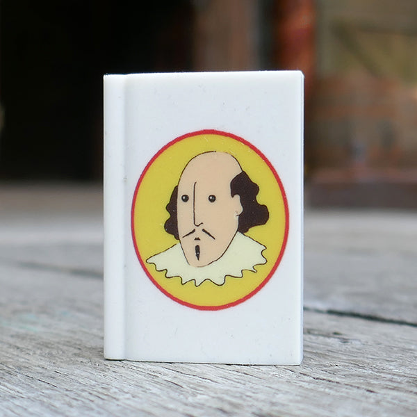 White eraser in the shape of a book printed with a cartoon portrait of Shakespeare on a yellow oval