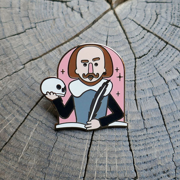 Cartoon metal pin badge of Shakespeare's torso with one hand holding a quill and the other a skull