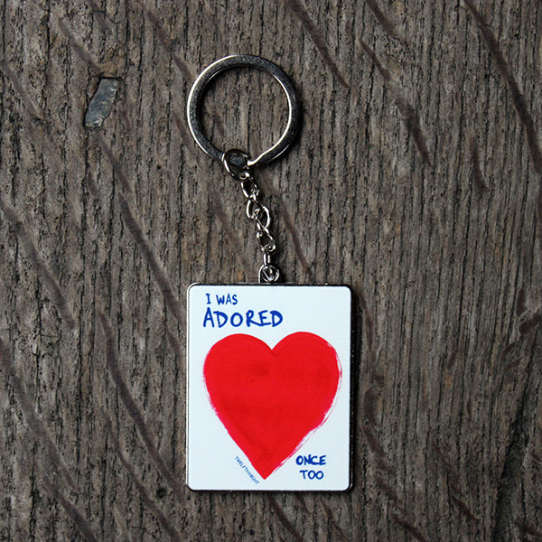 White rectangular keyring on silver metal backing, with red heart and blue text