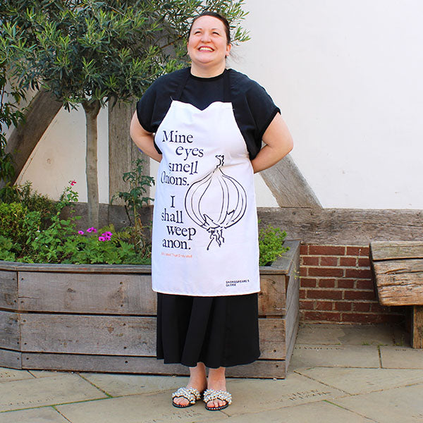 Person wearing a white apron with text and an onion graphic, standing outdoors.