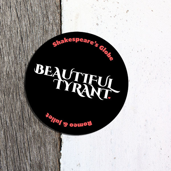 Round sticker with 'Beautiful Tyrant' text on a wooden surface