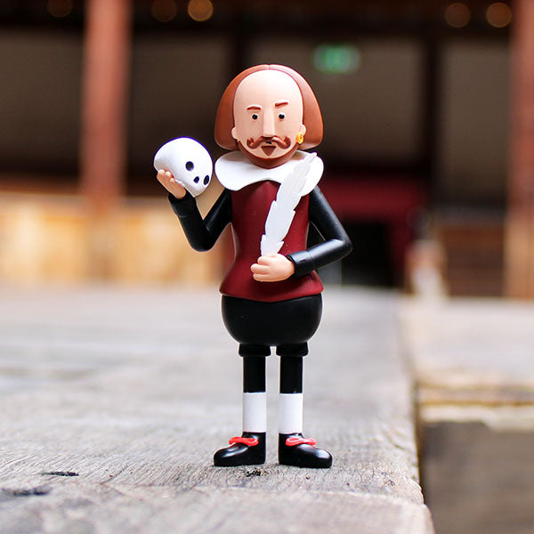 plastic figure of Shakespeare wearing a black and deep red costume holding a white skull and feather