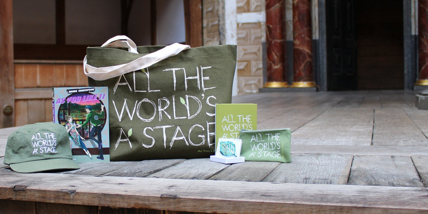 Wood panel stage floor with As You Like It sage green colour merchandise, left from right, baseball cap, paperback manga, tote bag, leaf brooch, hardback journal, purse