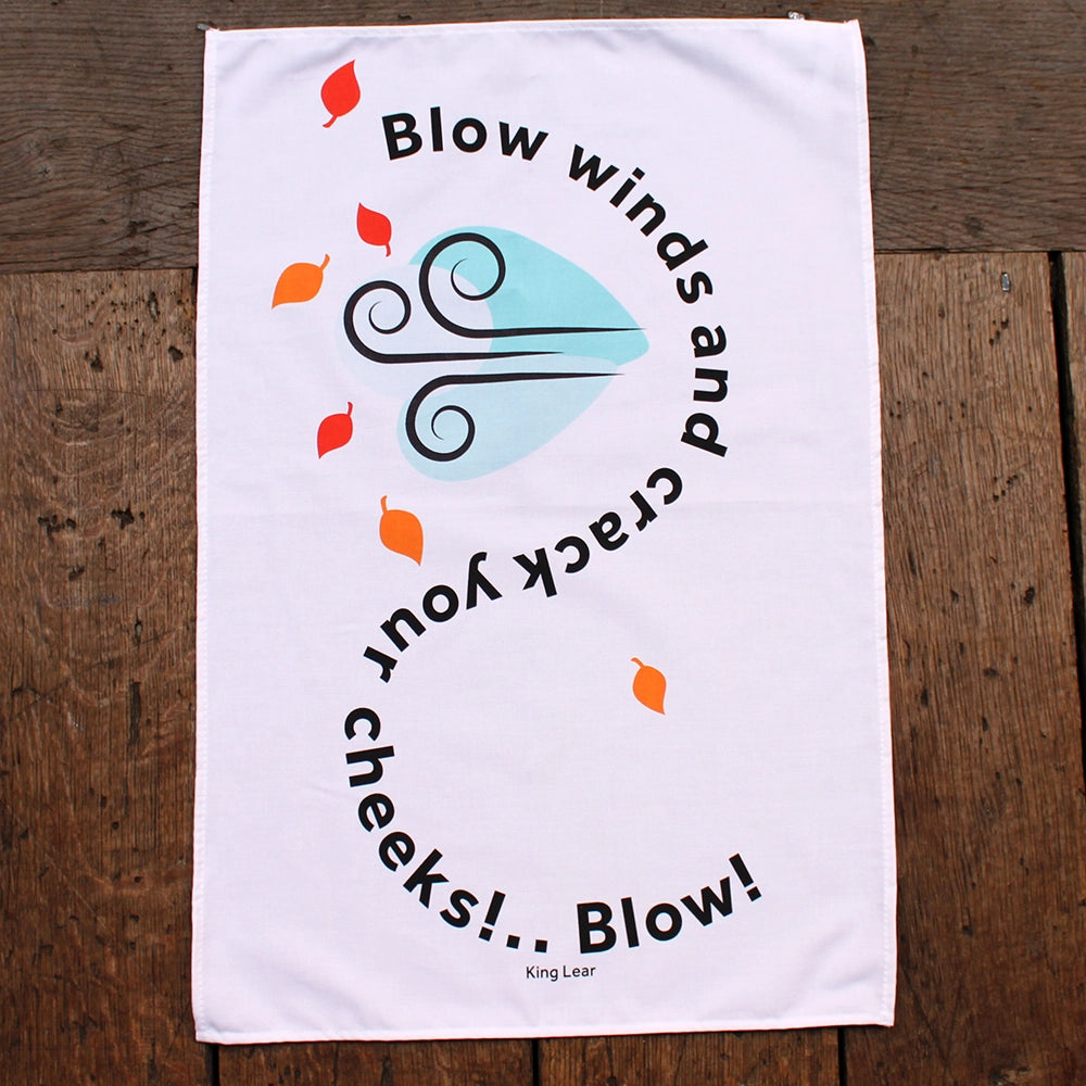 White tea towel printed with a swirling black quote  and red and orange leaves