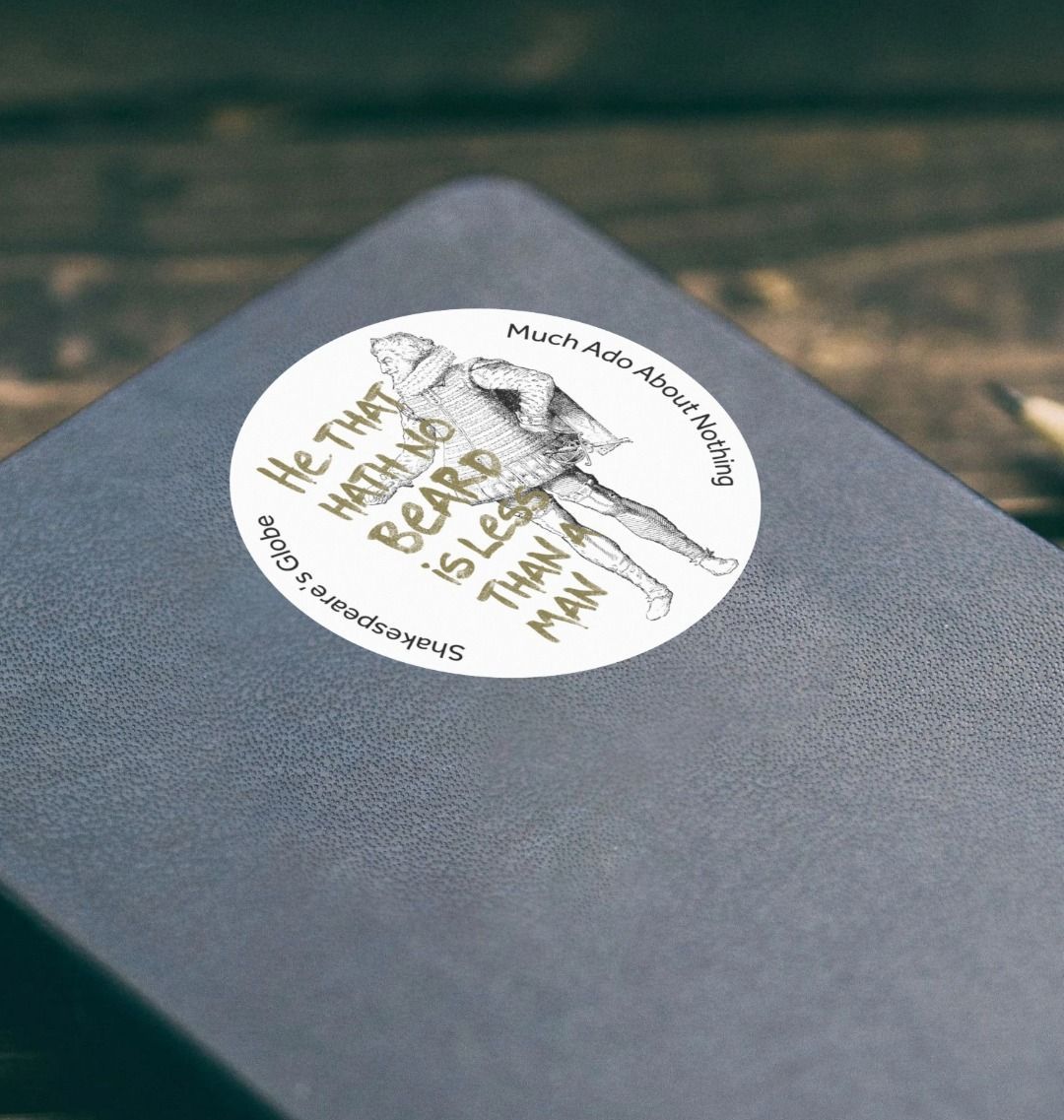 white circular sticker printed with a line drawing of a Tudor gentleman alongside a green quote, stuck on a black leather notebook