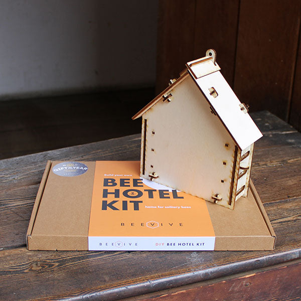 kraft card box with an orange label, a small plywood house sits on top of it
