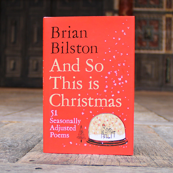 Book titled 'And So This is Christmas' by Brian Bilston on a wooden surface with a blurred background.