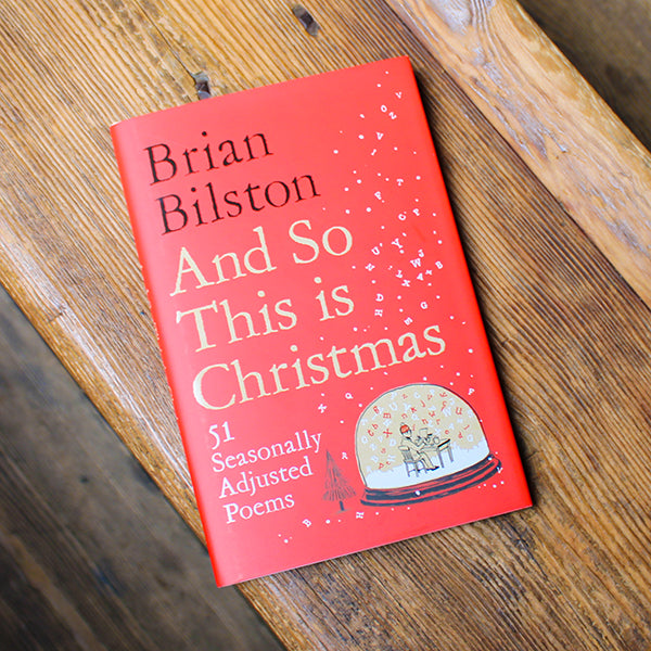 Book titled 'And So This is Christmas' by Brian Bilston on a wooden surface