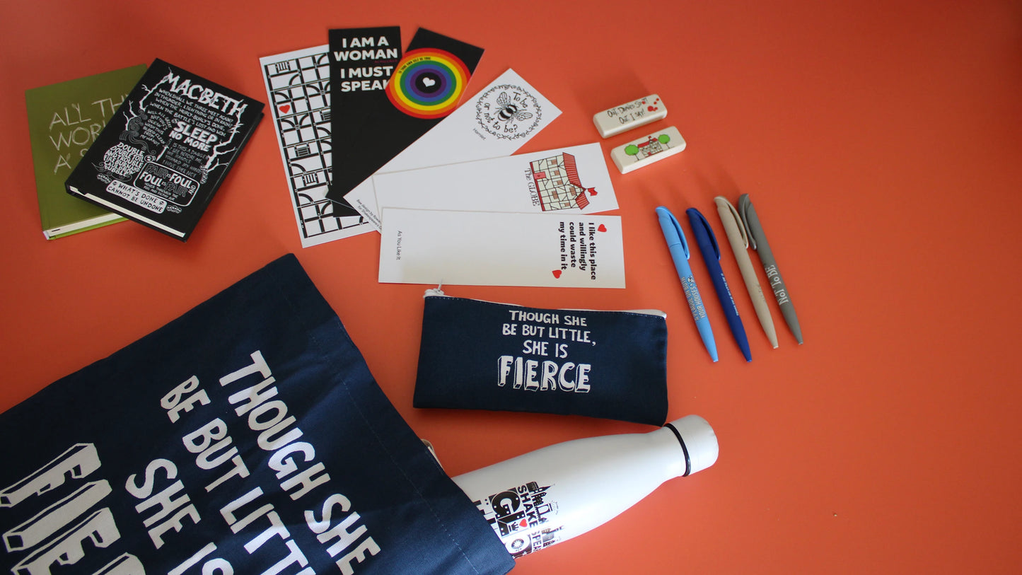 Shakespeare-inspired back-to-school stationery and accessories on a bright orange background, featuring a navy pencil case and tote bag printed with the A Midsummer Night’s Dream quote “Though she be but little, she is fierce,” a Macbeth notebook, literary postcards and bookmarks, colourful pens, erasers and a reusable water bottle.
