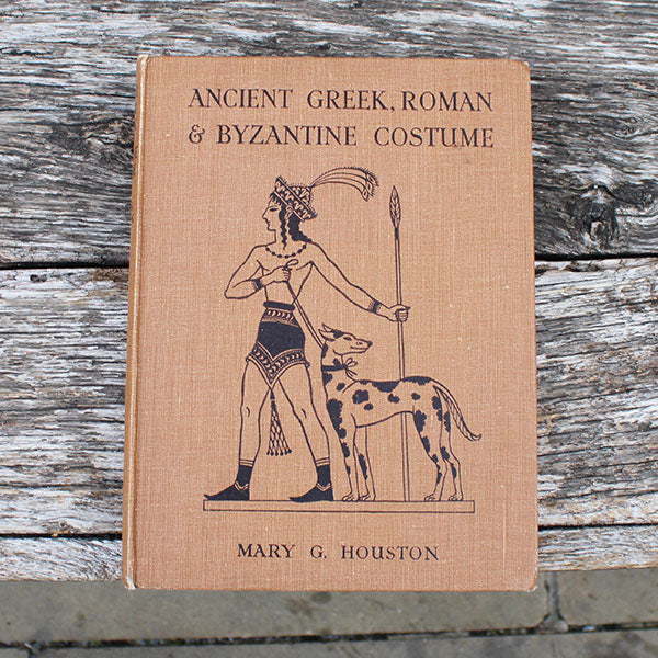 Book cover of 'Ancient Greek, Roman & Byzantine Costume' by Mary G. Houston on a wooden surface.
